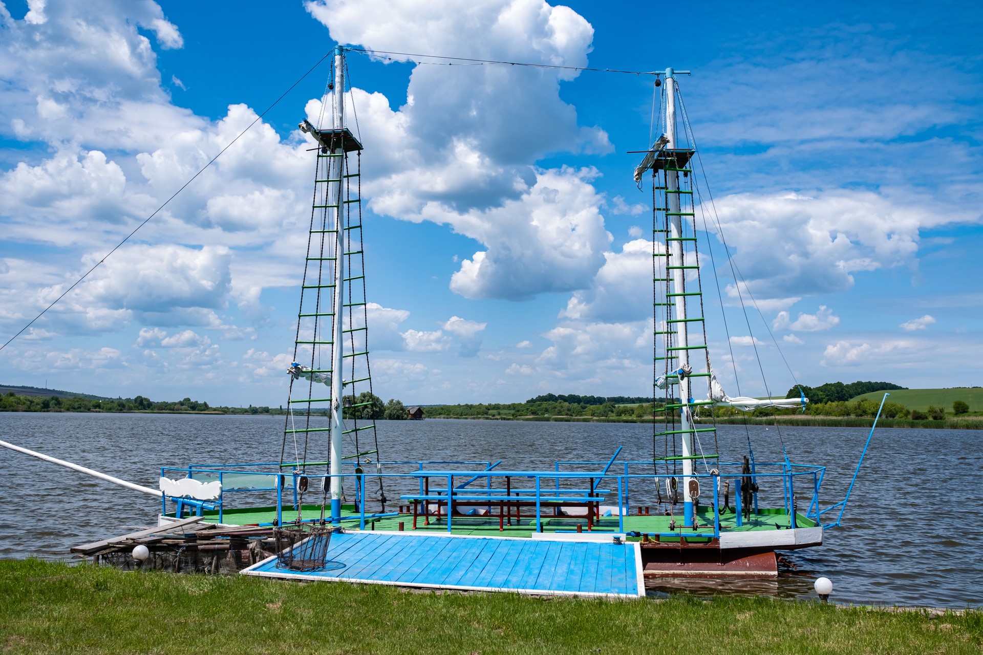 A homemade wooden boat with masts on iron barrels for fishing is moored to the shore of the lake.