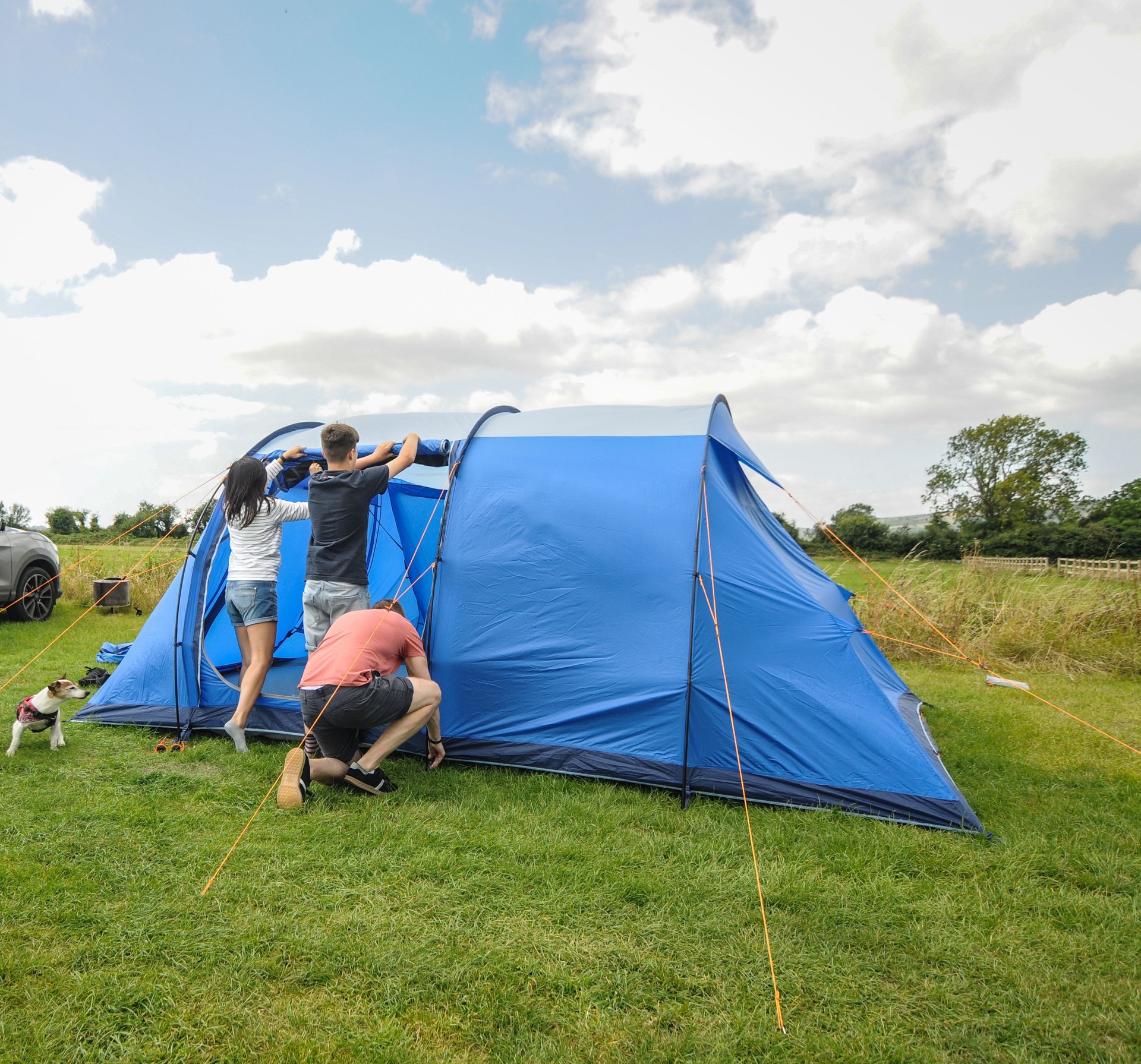 Family with dog setting up camping tent on a cloudy day at the campsite in Cheddar, Somerset, England